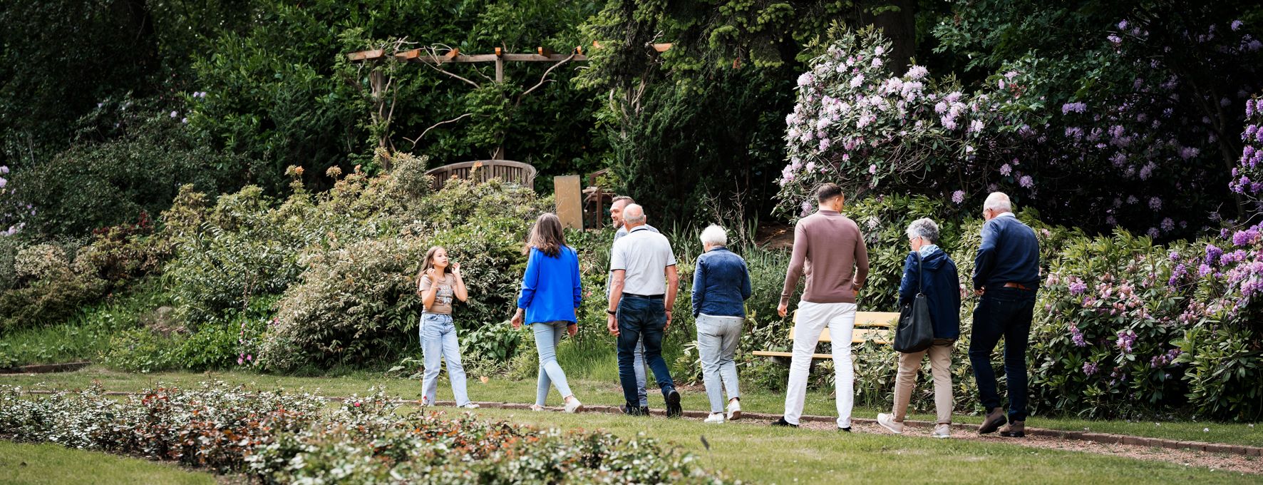 Jong en oud wandelen samen door een tuin vol bloeiende rododendrons